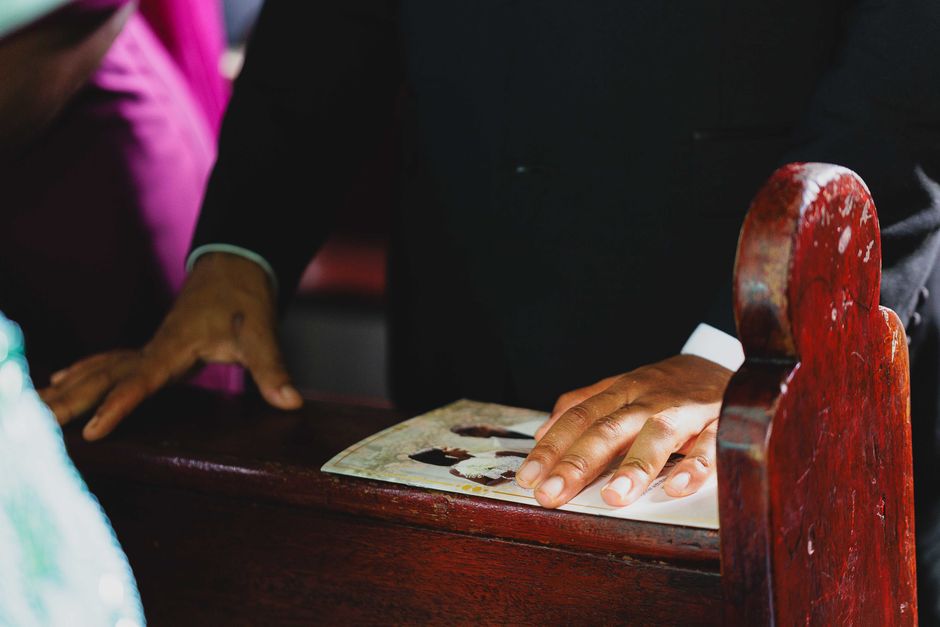 Close-up of hands on pew during a wedding ceremony, capturing intimate detail.