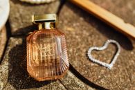 Close-up of Victoria's Secret Bombshell Soirée perfume with heart accessory on textured background.