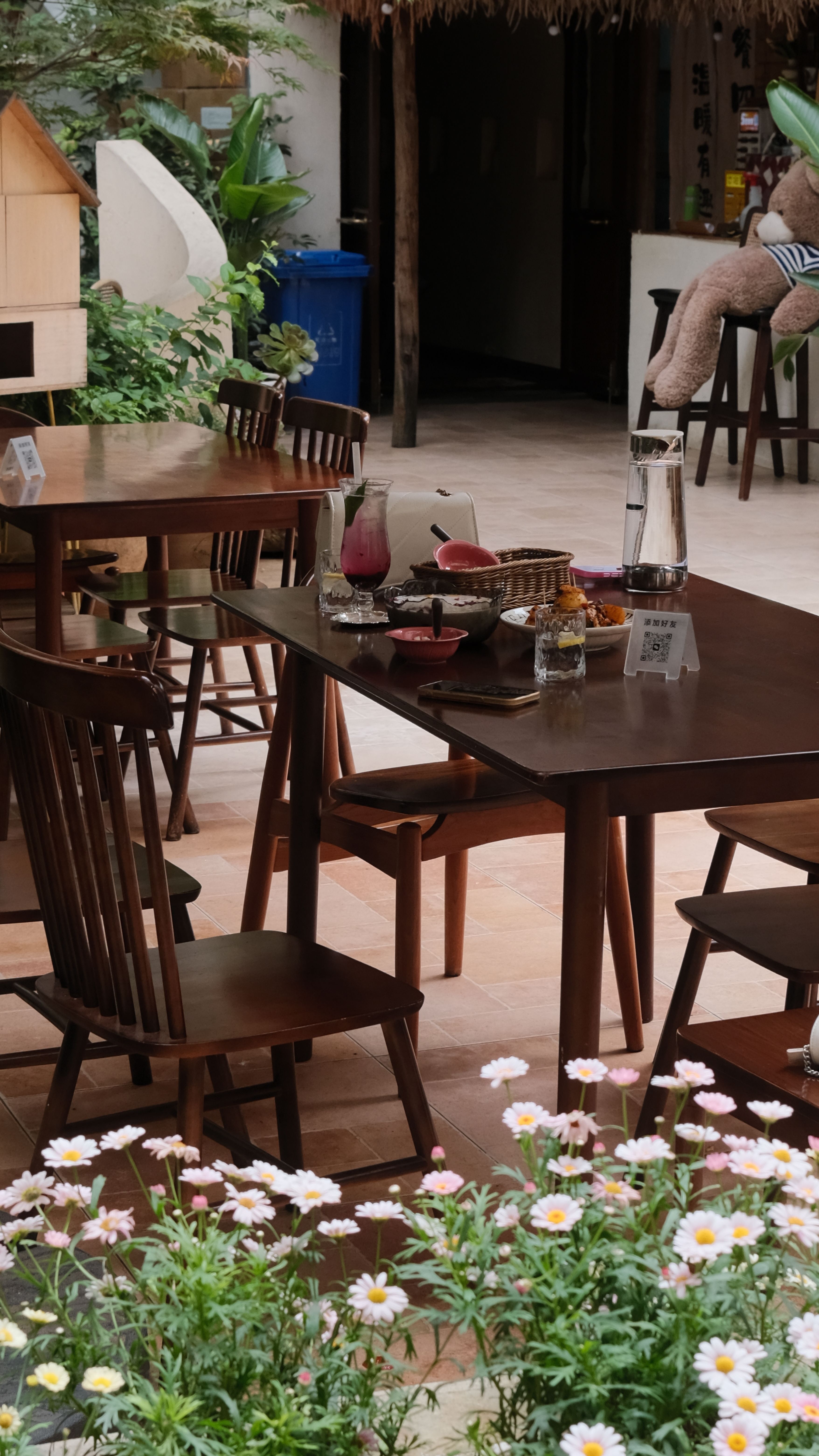 Inviting outdoor cafe scene with wooden tables, chairs, and floral foreground.