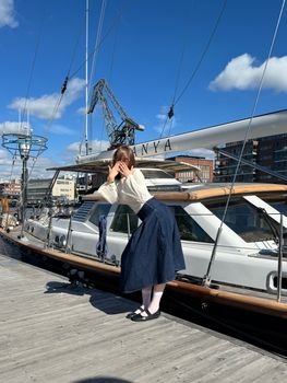 Woman posing casually on a yacht deck in a sunny marina.