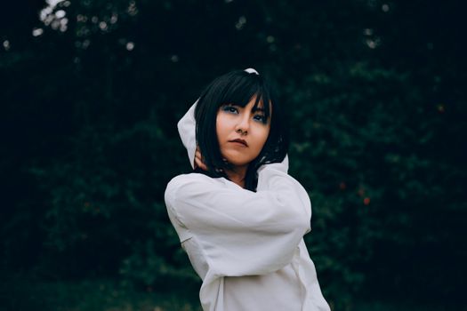 Contemplative woman with dark hair in a white top standing outdoors.