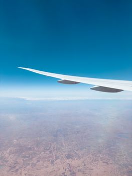 In-flight view of an airplane wing over a sprawling desert landscape under clear blue skies.