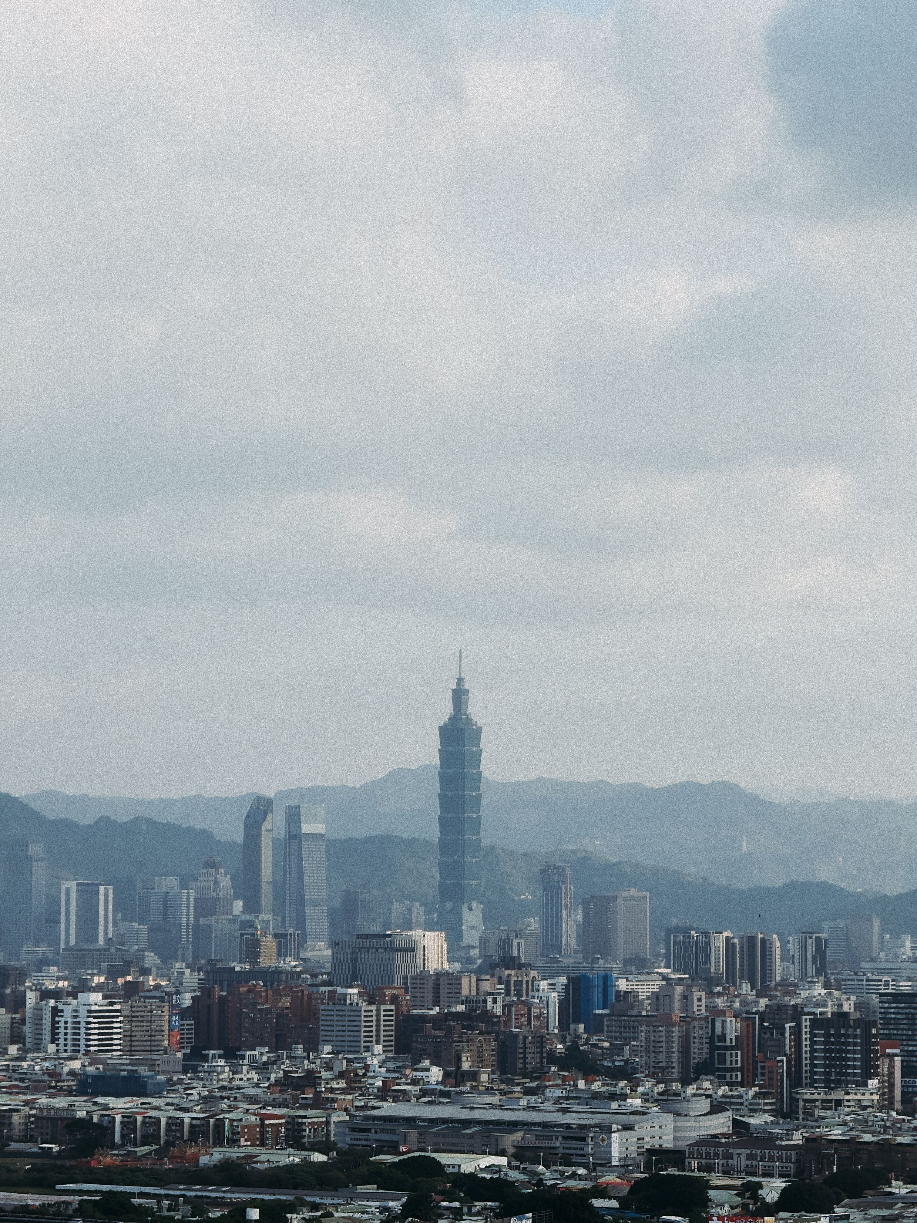 Aerial view of Taipei City showcasing the iconic Taipei 101 skyscraper against a mountainous backdrop.