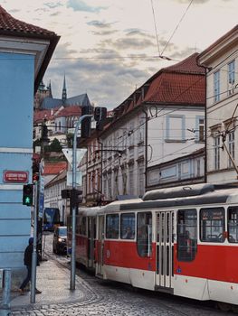 A red tram passes through a historic street in Prague, with the iconic Prague Castle in the background.