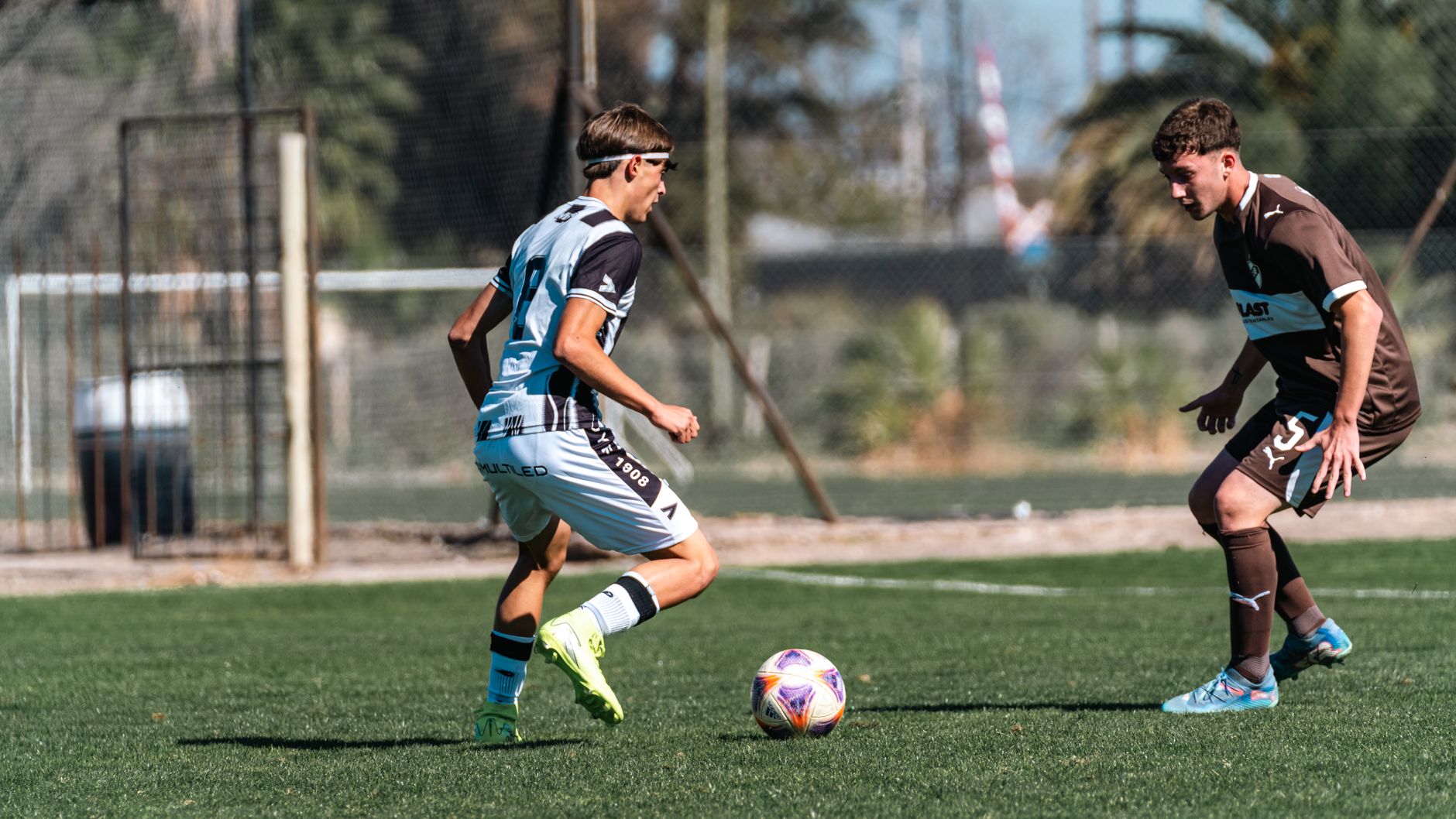 Two soccer players in action on an outdoor field during a sunny day.