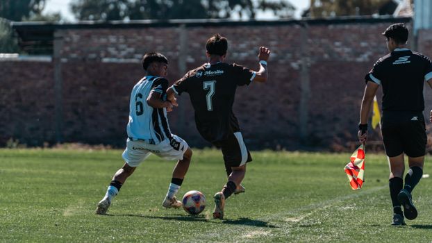 Soccer players in action on a sunny day at an outdoor match, with referee watching closely.