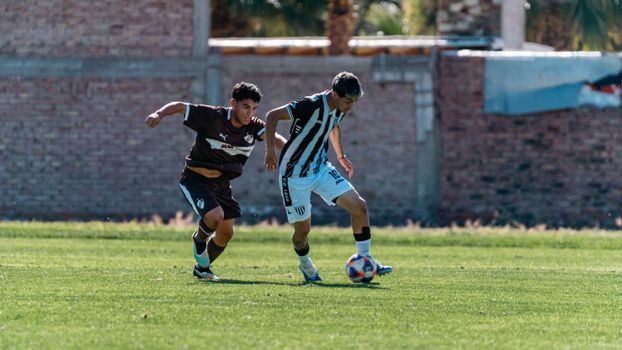 Two teenagers in soccer uniforms compete on a sunny outdoor field.