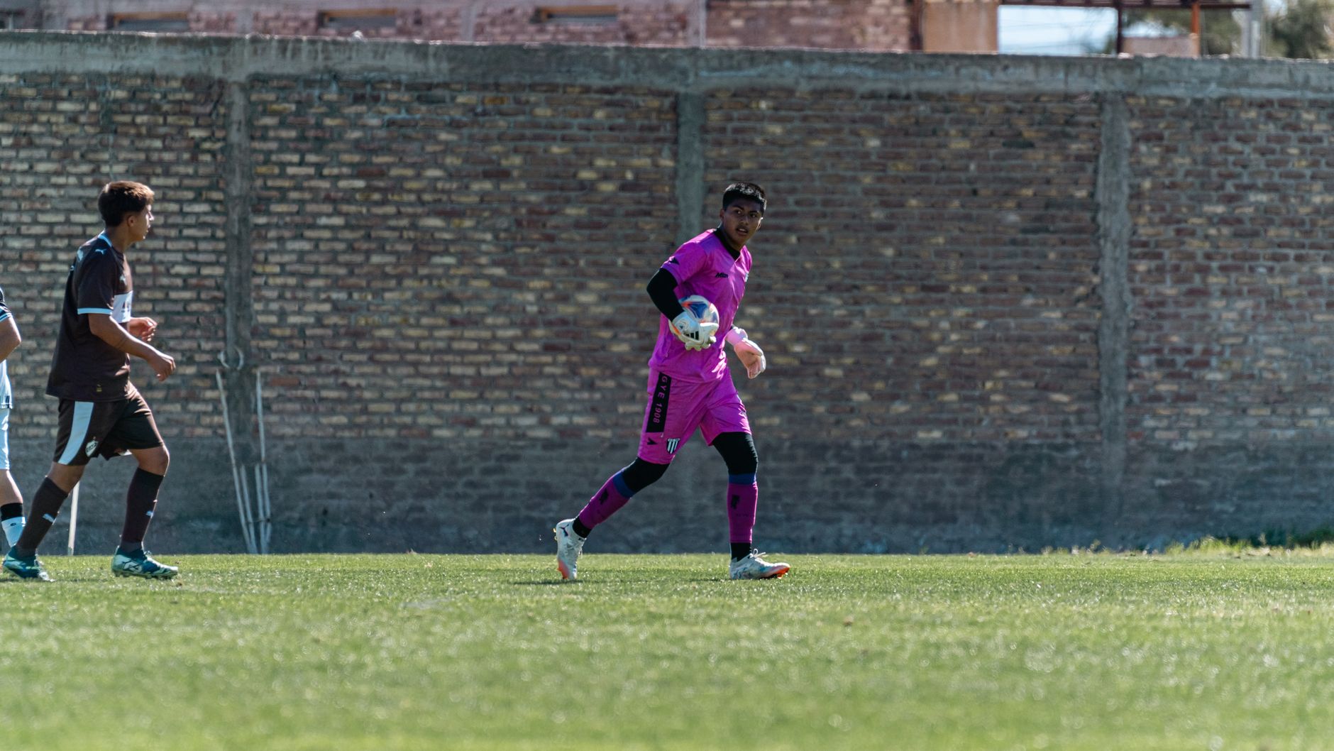 Goalkeeper in vibrant pink uniform during an amateur soccer match outdoors.