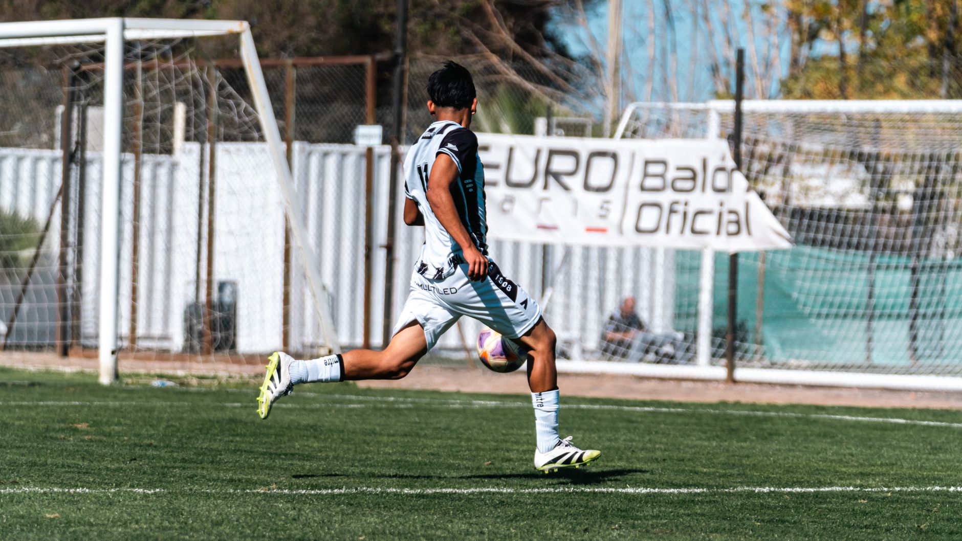 Action shot of a soccer player in mid-kick during a daytime match outdoors.
