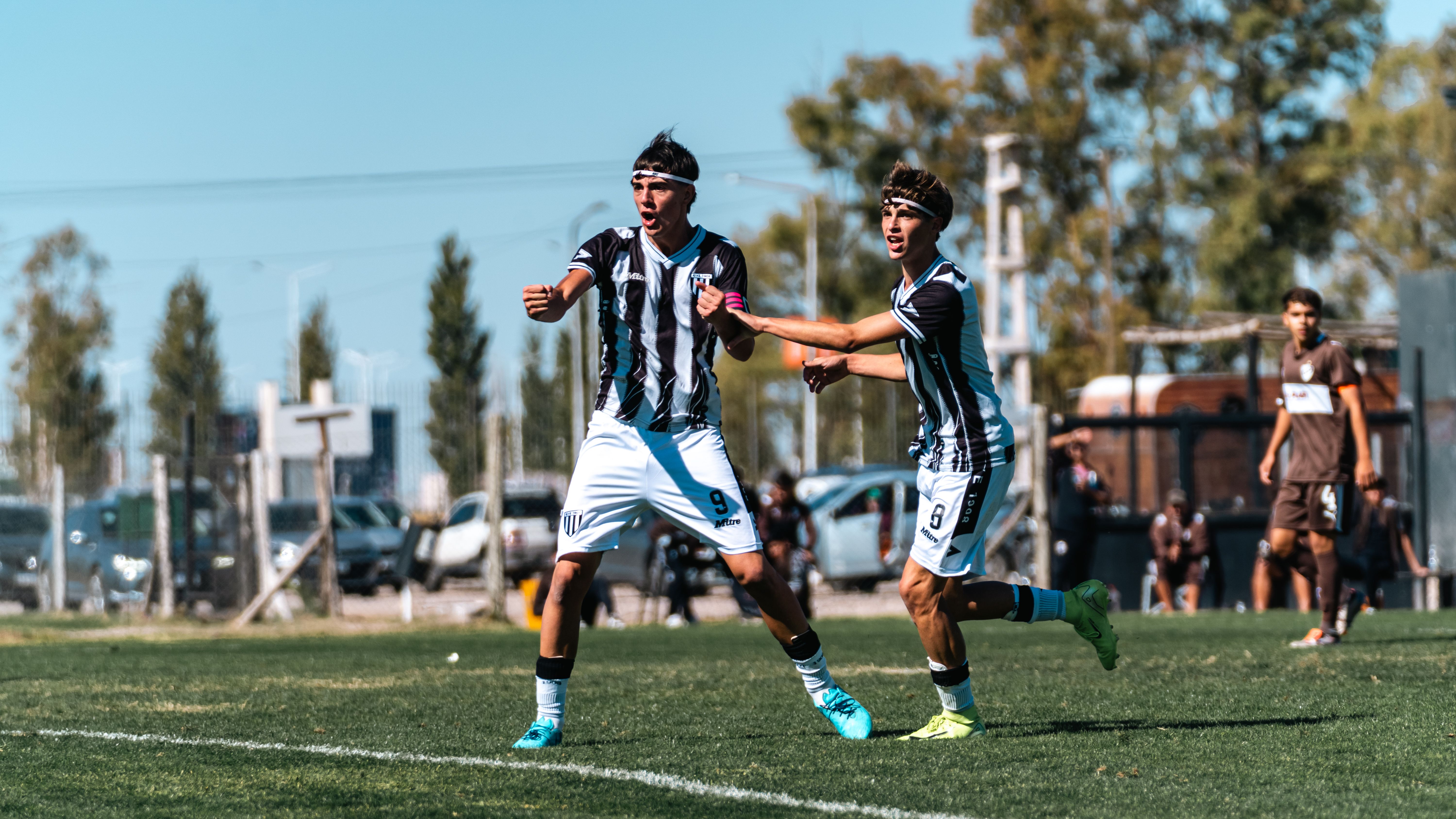 Two young soccer players celebrate a goal in an outdoor game on a sunny day.