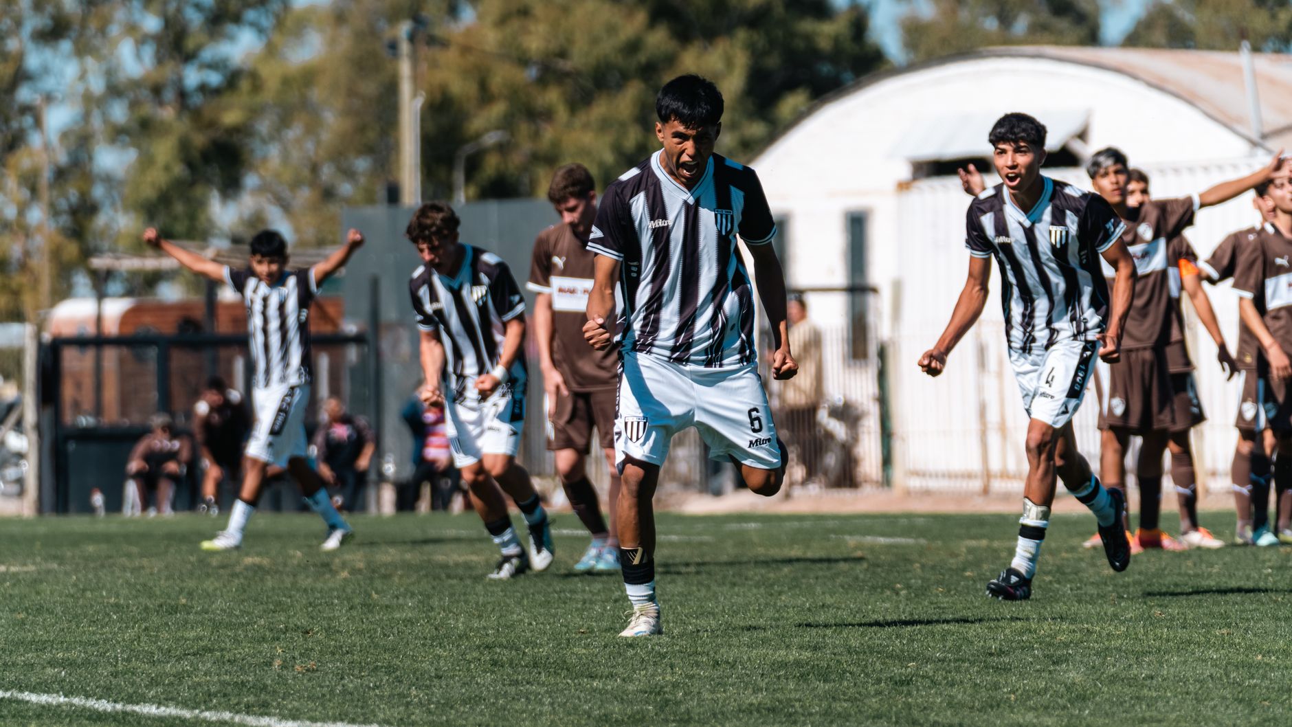 Excited players celebrate a goal during an intense youth soccer match outdoors.