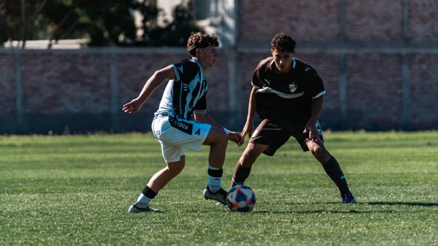 Two teenage soccer players competing fiercely on a grassy field during daylight.