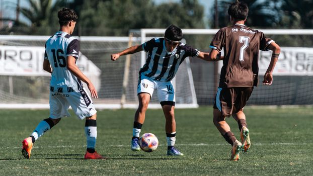Three young soccer players in action on a sunny field during a match.