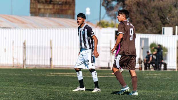 Two teenage soccer players in action on an outdoor field during a sunny day.
