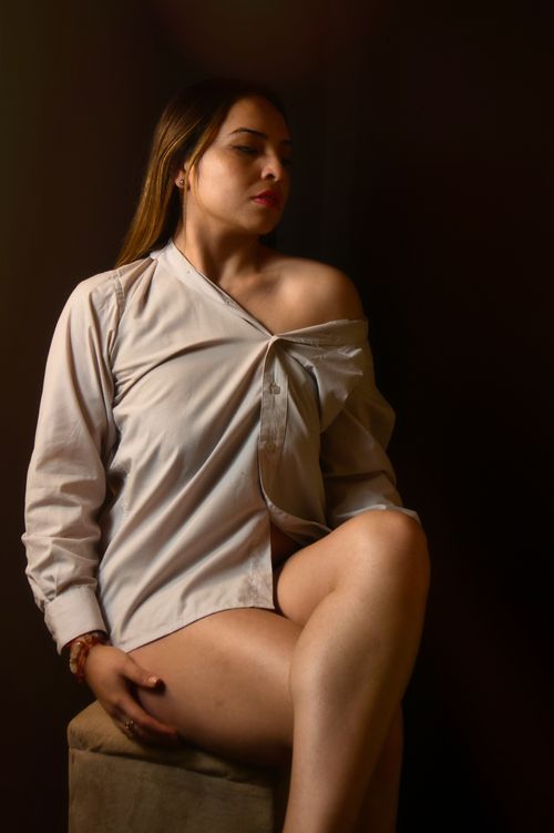 Free Portrait of a stylish woman in an off-shoulder shirt sitting indoors, capturing elegance and modern fashion. Stock Photo