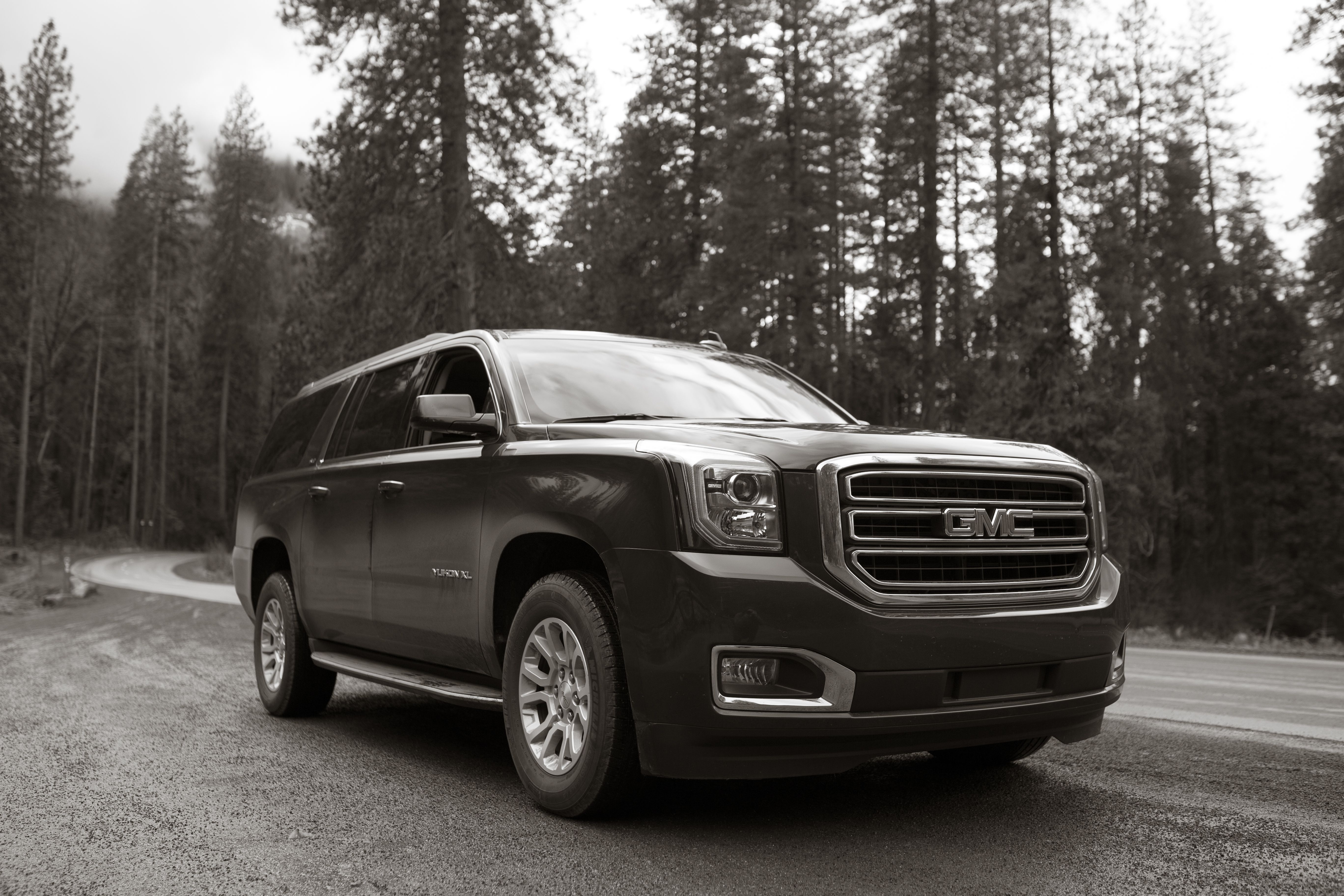 Black and white image of a GMC Yukon XL parked on a winding forest road.