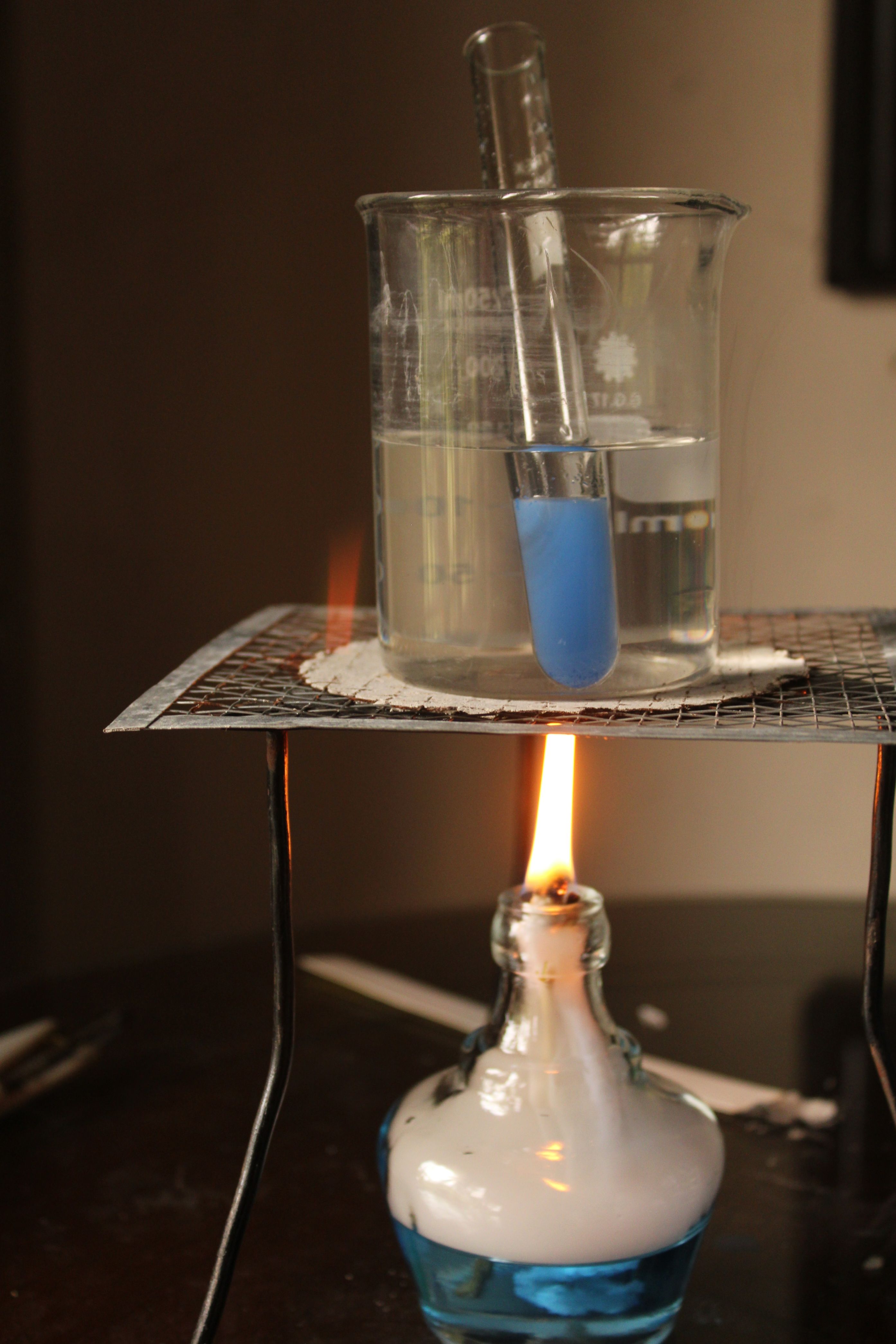Laboratory setup with a beaker heated by a Bunsen burner, illustrating a chemical experiment.