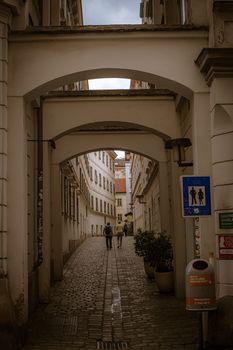 A narrow, cobbled alleyway in Europe with two adults walking under a classic arch.