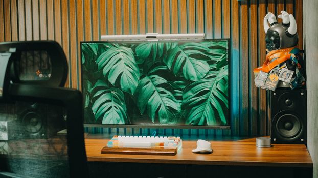 Wooden desk with monitor displaying green leaves, keyboard, and decor in modern home office.