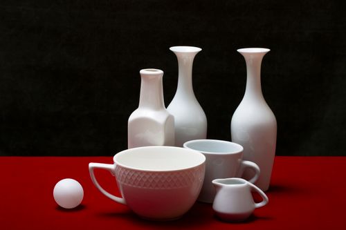 Free A sophisticated still life showcasing white porcelain vessels on a red surface with a black background. Stock Photo
