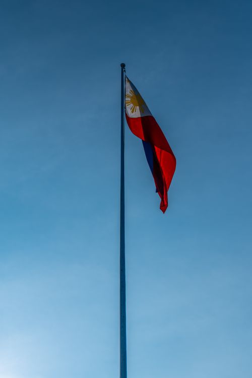 Free The Philippine flag waving on a tall pole set against a clear blue sky, symbolizing national pride. Stock Photo