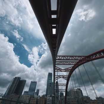 Striking perspective of a bridge leading to a city skyline under dramatic cloudy sky.