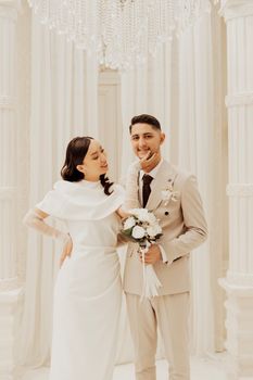 Smiling bride and groom pose elegantly in a bright wedding venue.