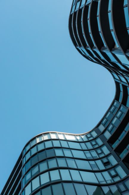 A low-angle shot of a contemporary, curvilinear skyscraper with glass facade in Melbourne, Australia against a clear blue sky.