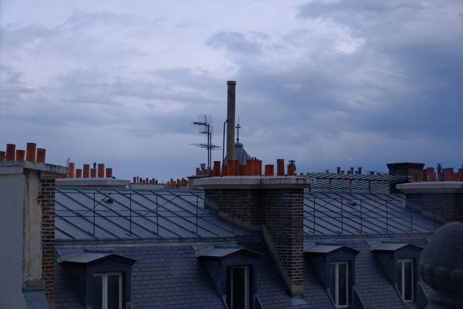 Scenic view of Paris rooftops and chimneys under a cloudy dusk sky.