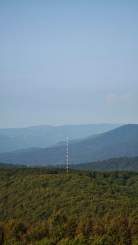 A panoramic view of a verdant mountain range with visible communication tower under clear blue skies.