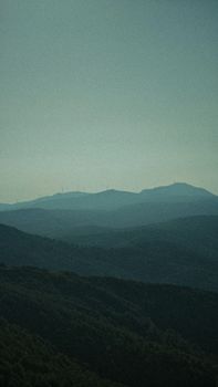 Sunlit mountain range with wind turbines on a misty day, providing a serene and eco-friendly vibe.