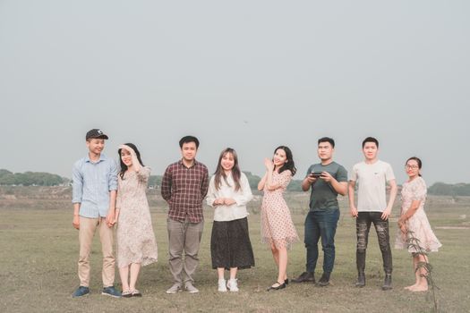 Full body cheerful Asian men and women standing together on meadow in highlands smiling at camera