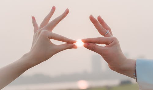 Crop unrecognizable friends touching glowing sun with hands while standing under sky at sunset