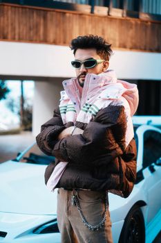 Fashionable man wearing a winter jacket and sunglasses, posing confidently outdoors.