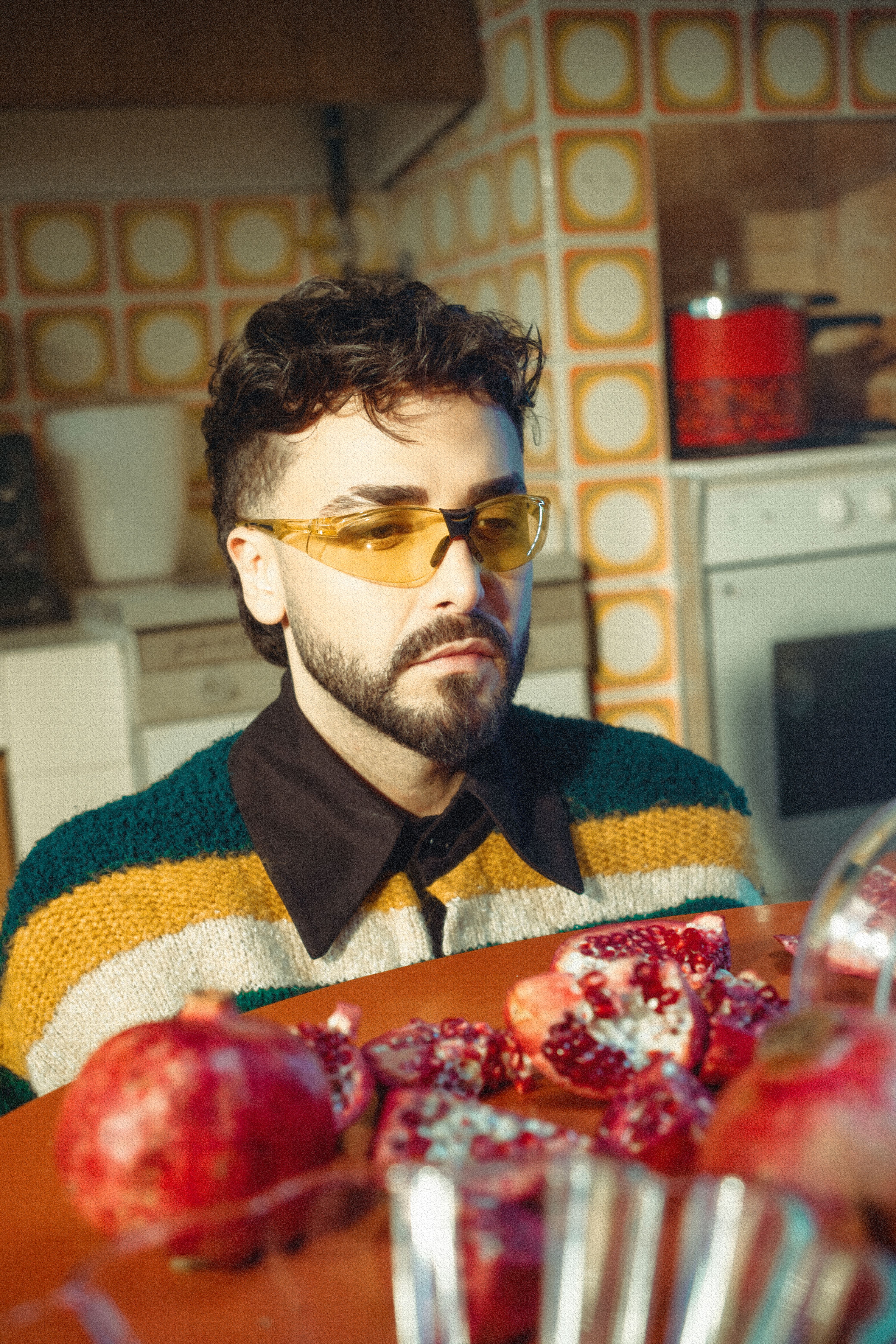 Portrait of a man in a colorful sweater and yellow glasses with pomegranates in a retro kitchen.