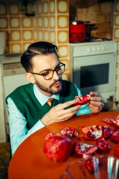 A man savors a fresh pomegranate in a retro kitchen setting, exuding a nostalgic vibe.