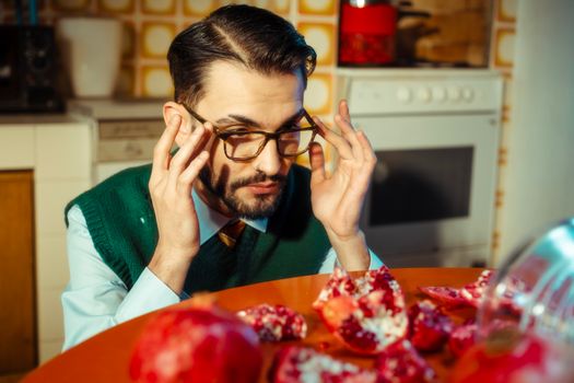 A man in glasses examines pomegranates in a vintage-style kitchen setting.
