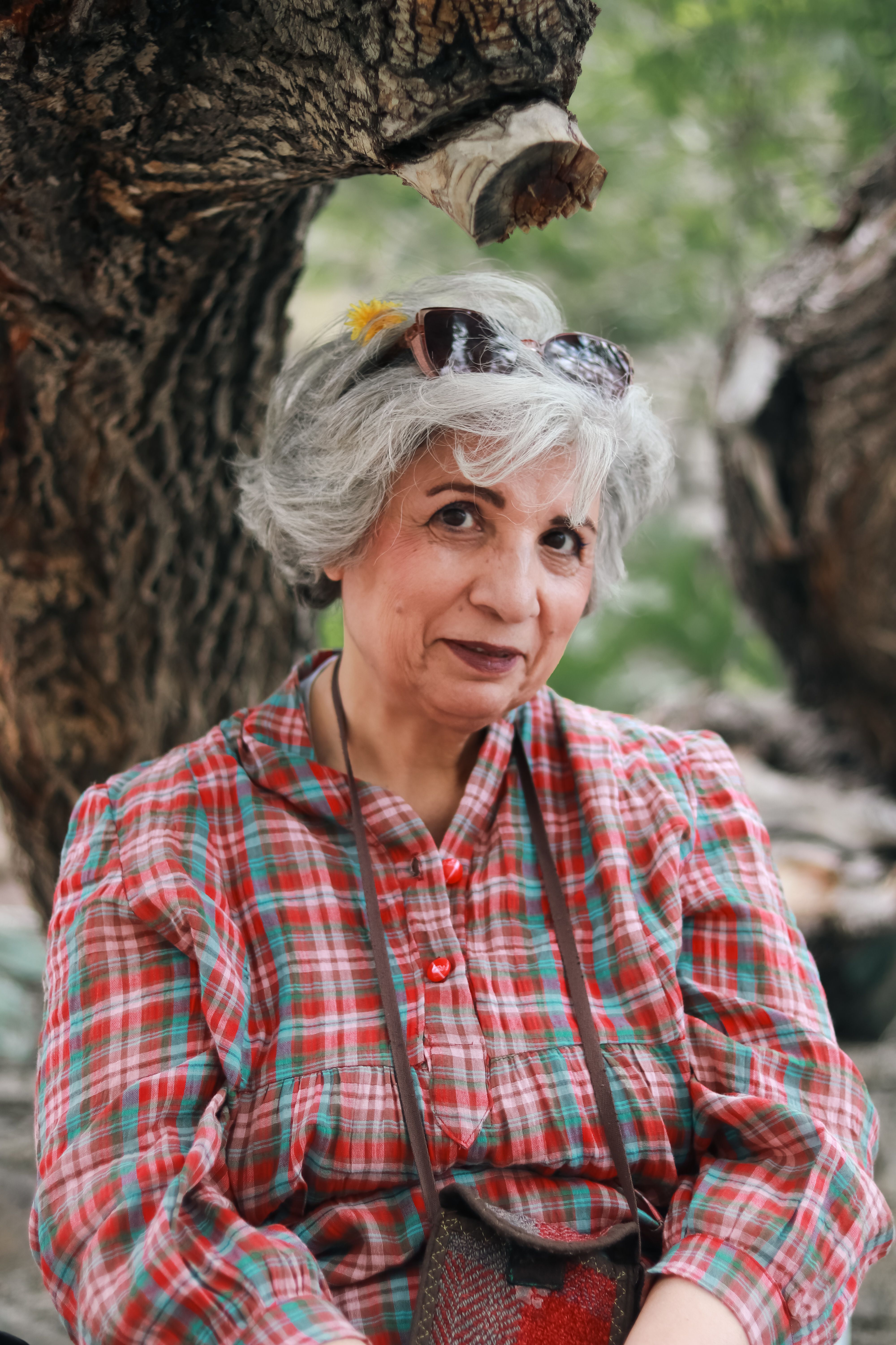 Charming senior woman in plaid shirt enjoying a peaceful moment in a forest setting.