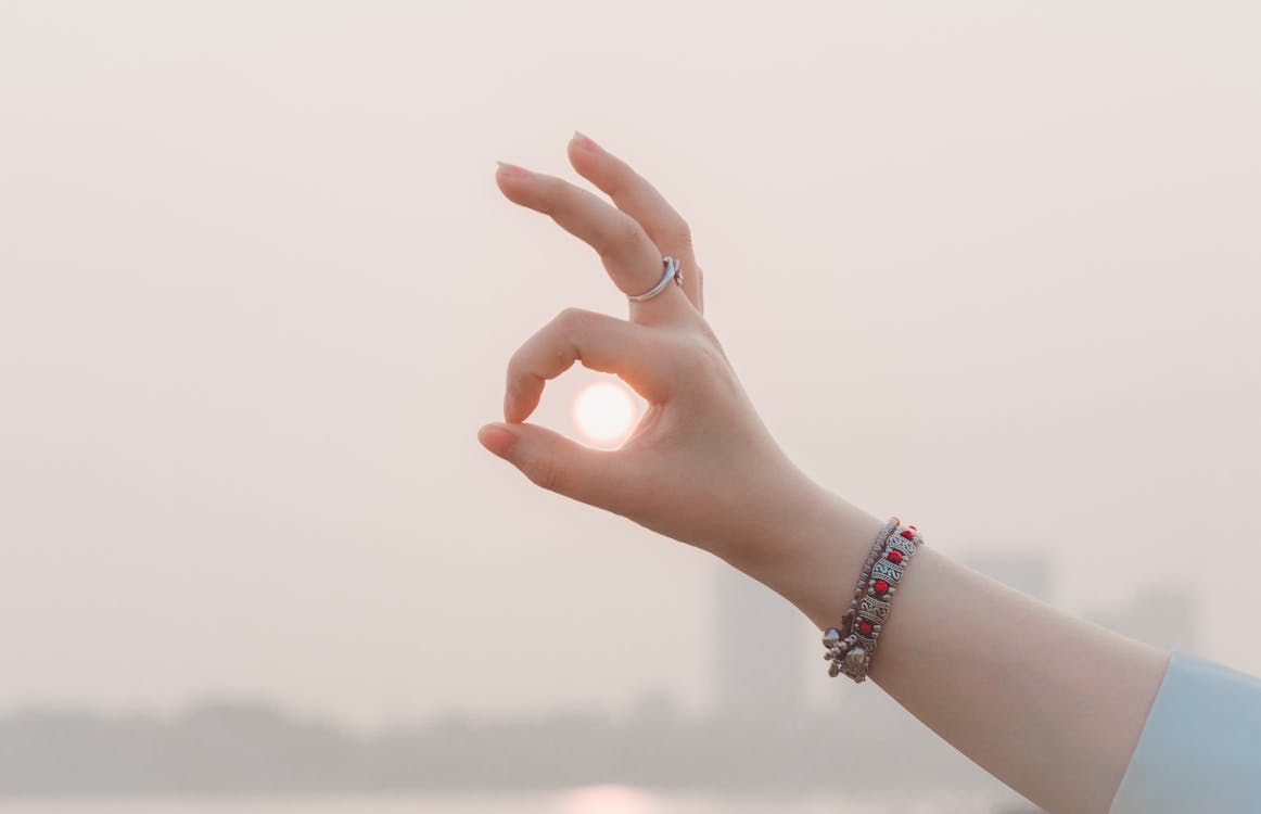 Crop woman showing okay gesture touching sun on street