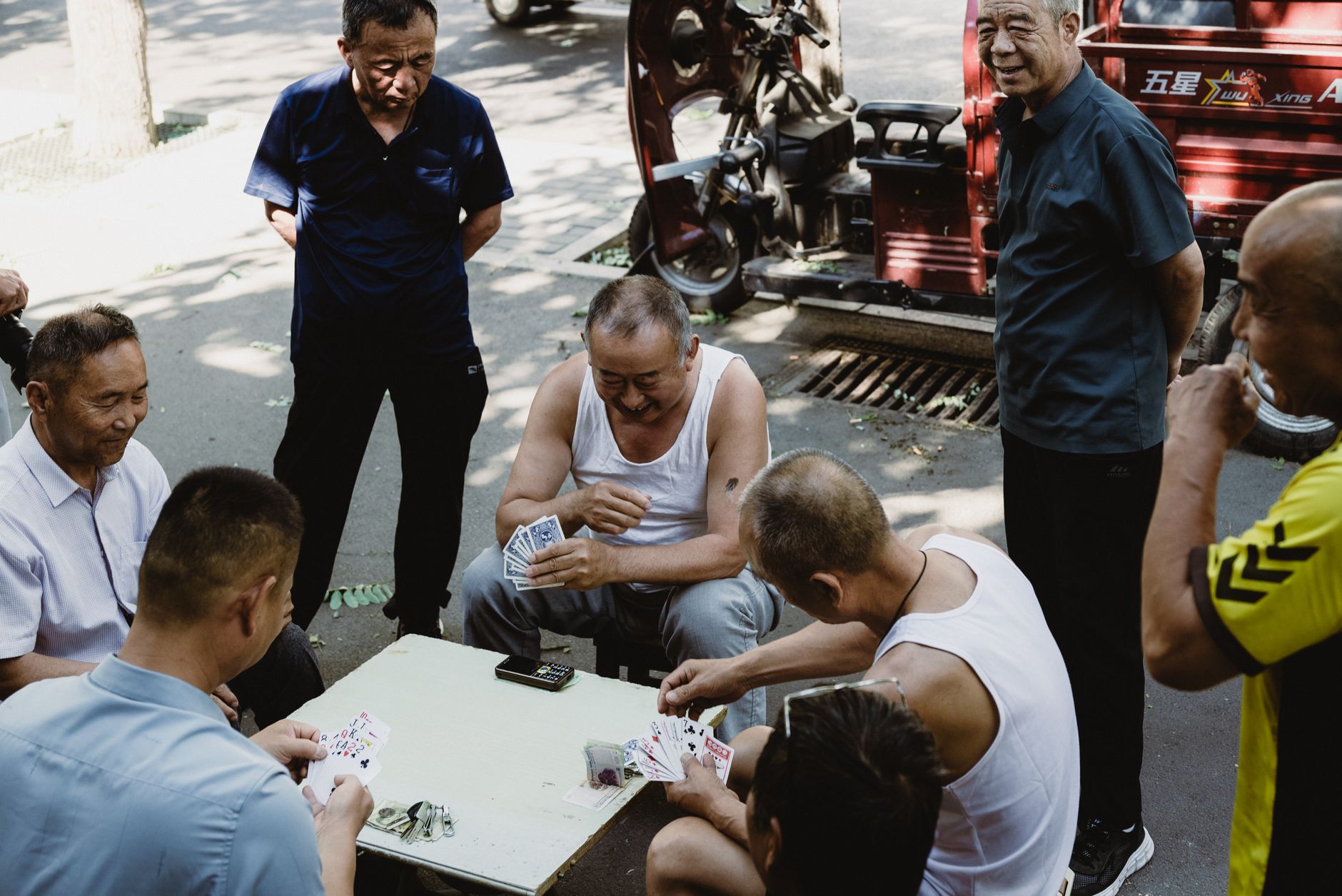 A group of adult men engaged in a card game outdoors during the day, conveying a relaxed social atmosphere.