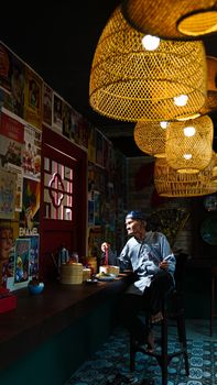 Elderly man dining in vintage-themed Indonesian restaurant with dim lighting.