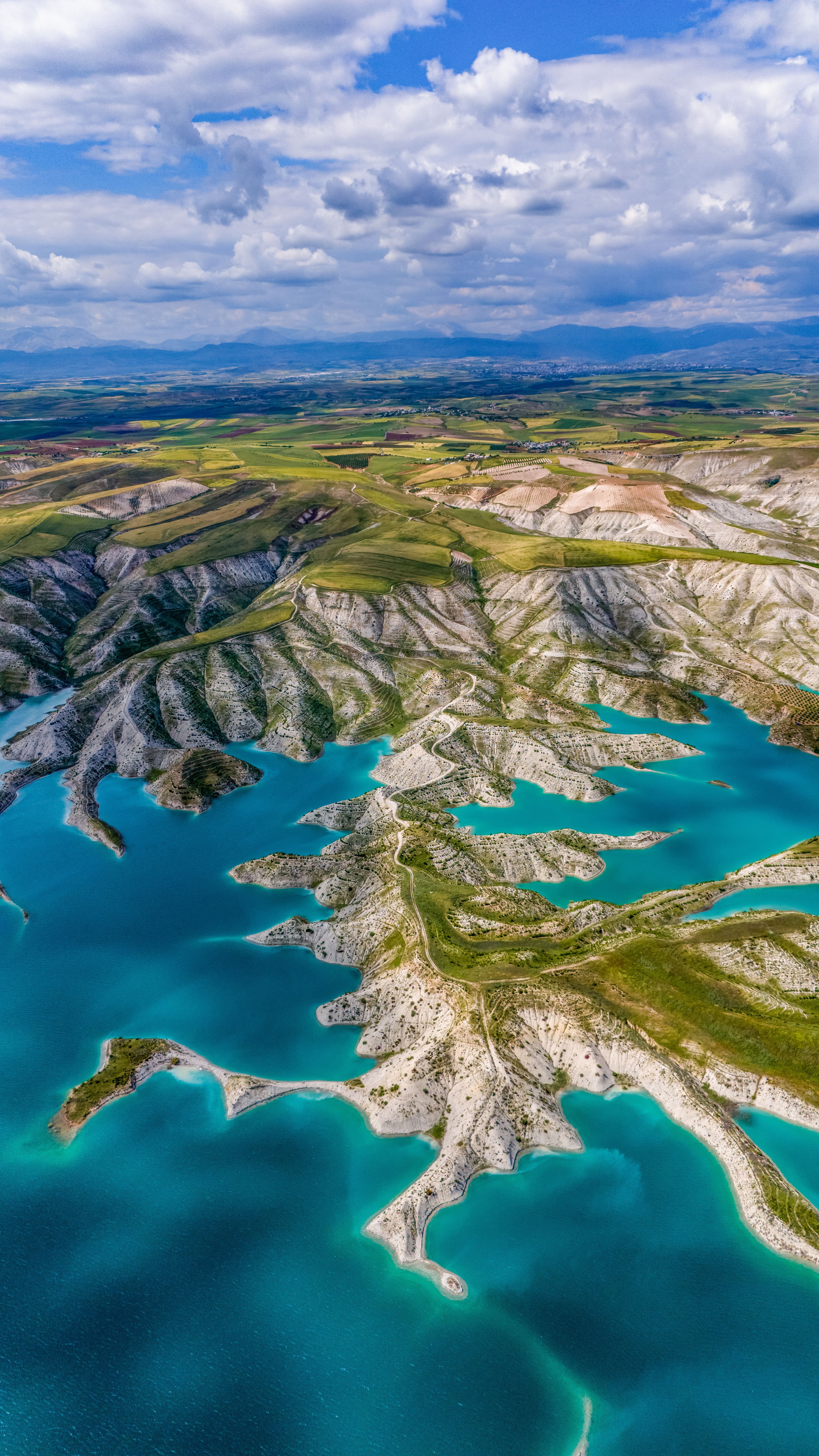 Stunning aerial image of a turquoise lake amidst hills, showcasing natural beauty under a partly cloudy sky.