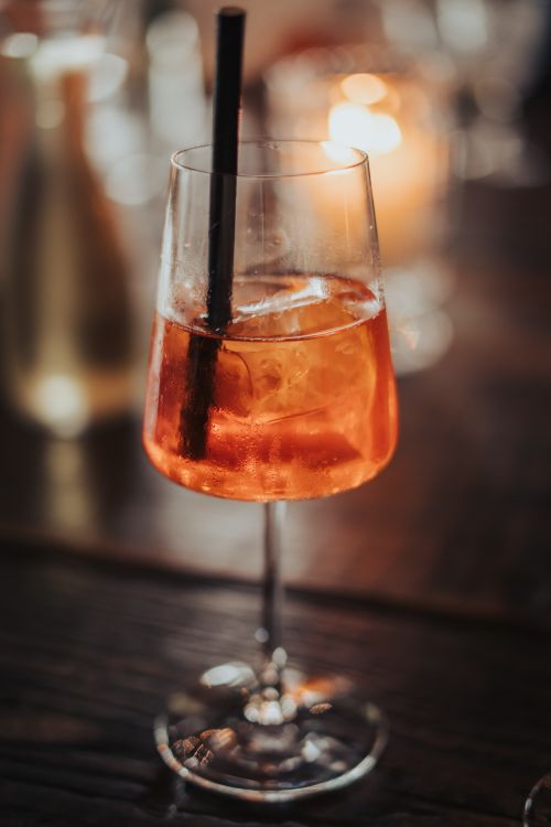 Free Close-up of an Aperol Spritz cocktail with ice and straw on a wooden table, warmly lit. Perfect for lifestyle or food photography. Stock Photo