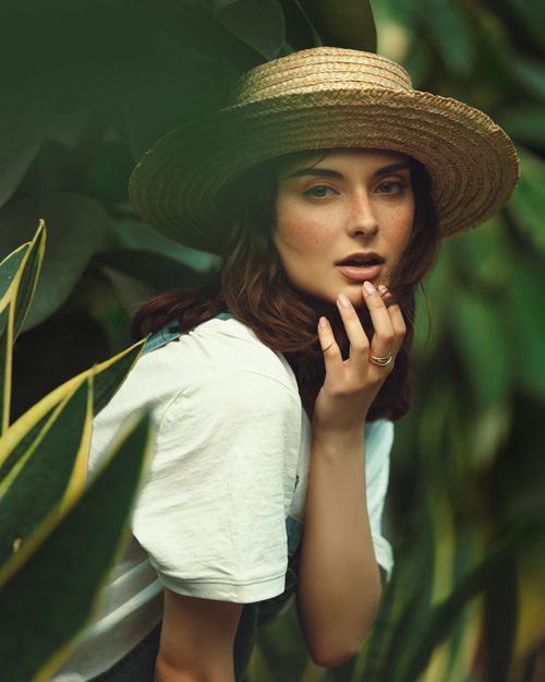 Free Portrait of a woman in a straw hat surrounded by lush greenery, exuding fashion and elegance. Stock Photo