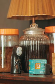 A rustic shelf features a unique figurine alongside vintage jars and a warm-toned lamp, creating a cozy atmosphere.