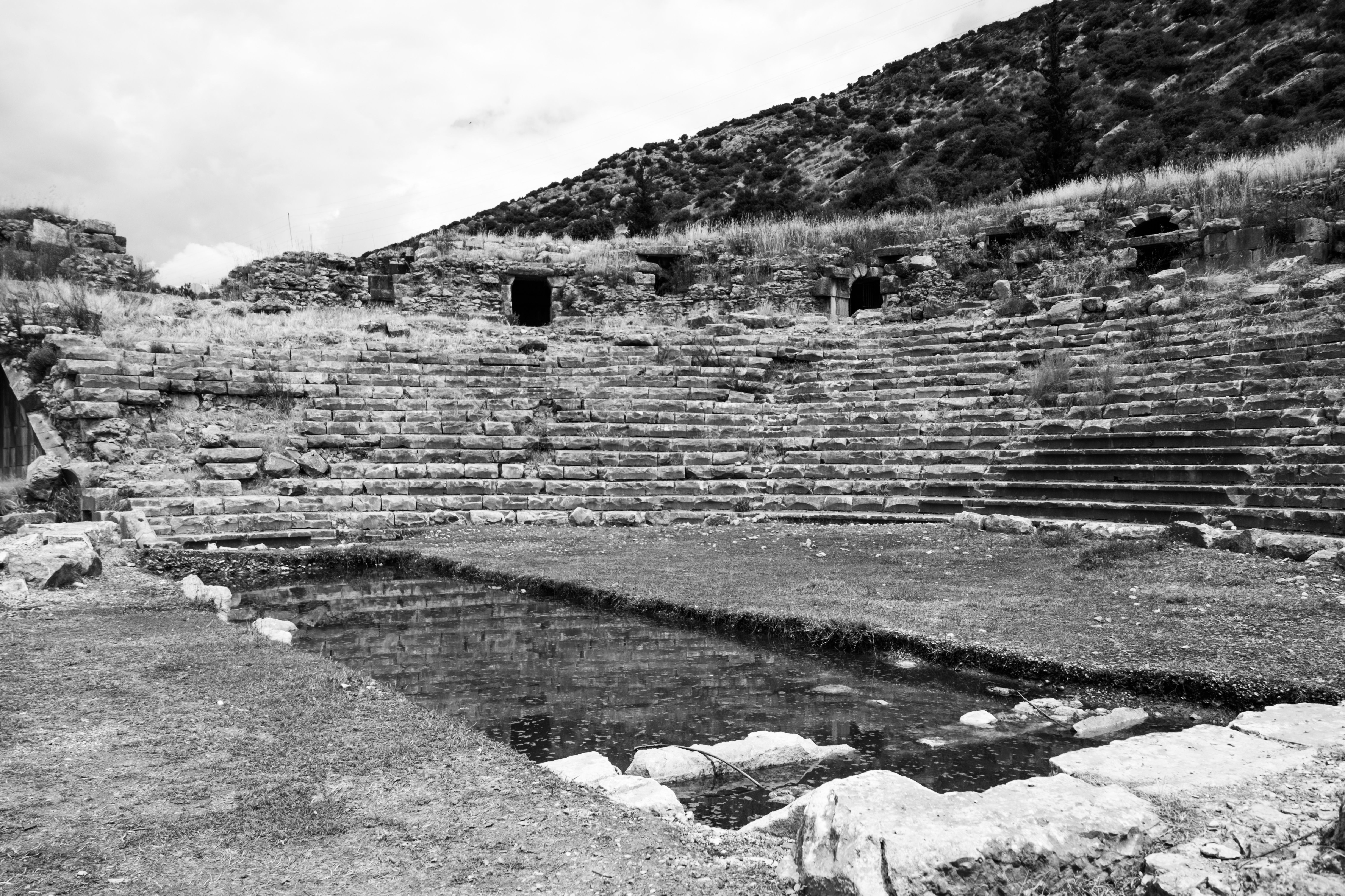 Taş basamakları ve kalıntısı korunan antik bir tiyatronun siyah beyaz fotoğrafı.
