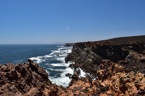 Free Rugged coastline along South Africa showing dramatic cliffs and crashing waves under a clear blue sky. Stock Photo