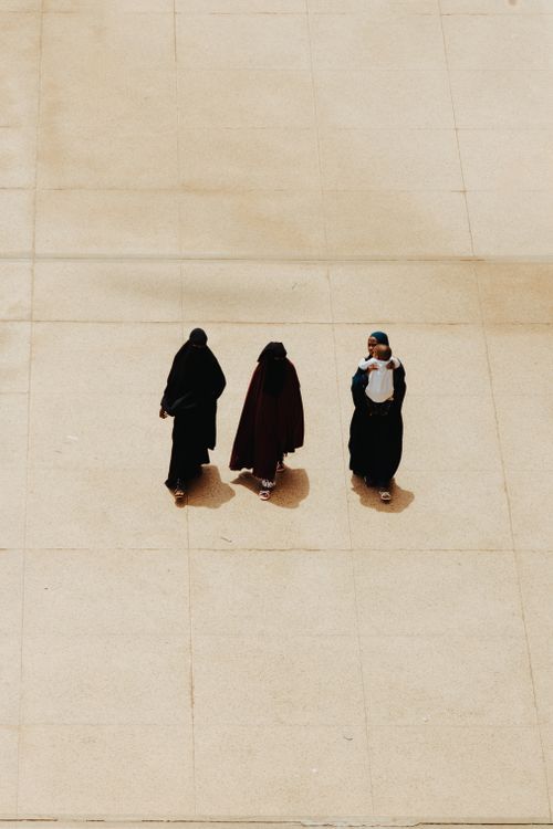 Free Three women wearing hijabs walk on a sunlit concrete surface, captured from above. Stock Photo