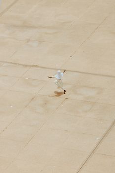 A solitary person joyfully dances across a vast, empty pavement in daylight.