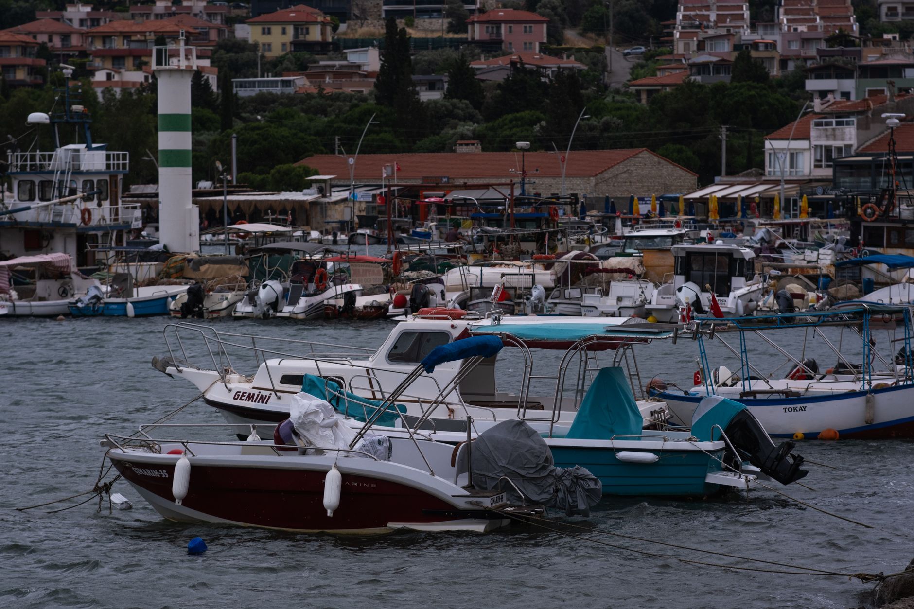 Boats docked at the scenic marina in Foça, İzmir, Türkiye under cloudy skies.